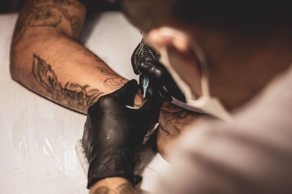 tattoo artist applying a tattoo on man's arm