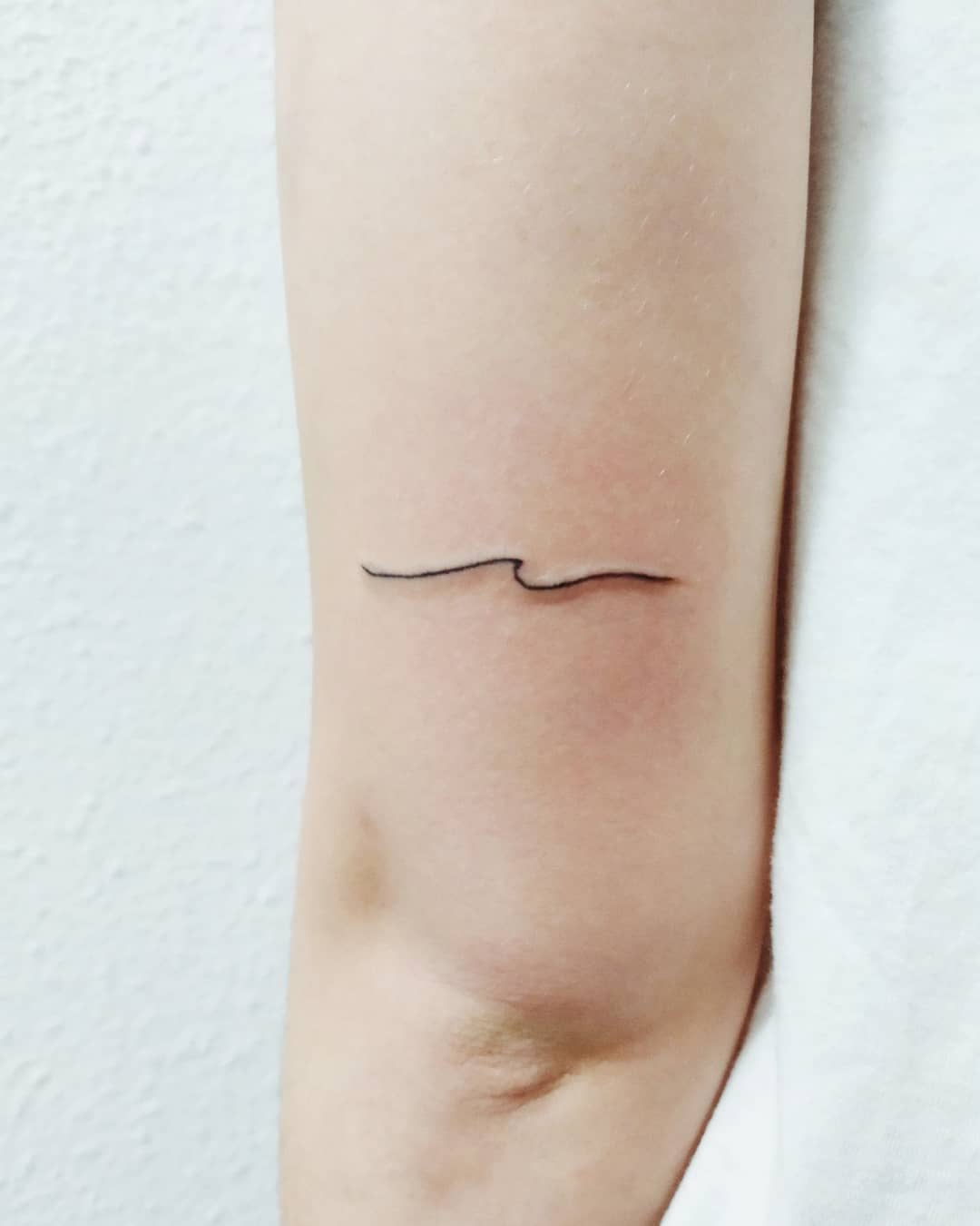 Single needle wave tattoo on the inner forearm.